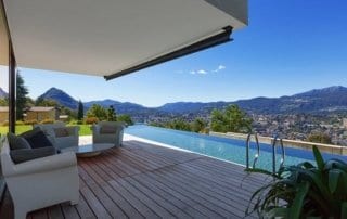 Modern balcony with outdoor seating and infinity pool overlooking mountains and cityscape.